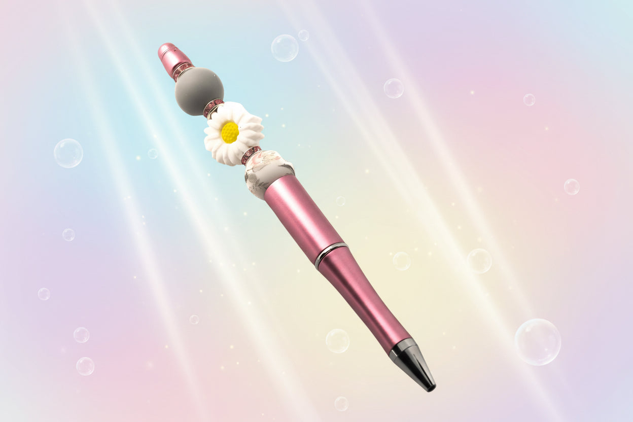 A pink metallic pen with a white daisy shaped bead, a plain grey bead, a pink an grey floral bead with pink rondelles
