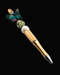 A decorative pen with a blue floral butterfly bead, daisy patterned bead, white bead and green, pink and blue glitter rondelles
