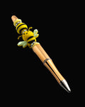 A gold pen with yellow oval silicon beads, a black and yellow striped bead and a bee shaped bead all separated by glitter rondelles