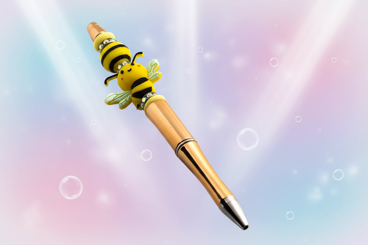 A gold pen with yellow oval silicon beads, a black and yellow striped bead and a bee shaped bead all separated by glitter rondelles