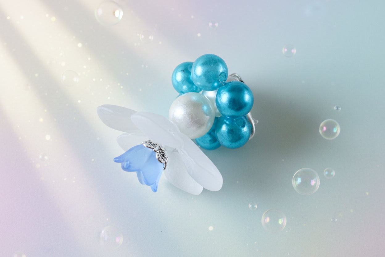 A stunning white flower bead takes centre stage, encircled by shimmering teal pearlescent beads that create a mesmerising spinning effect. The soothing tactile motion helps with focus and stress relief while looking absolutely magical.