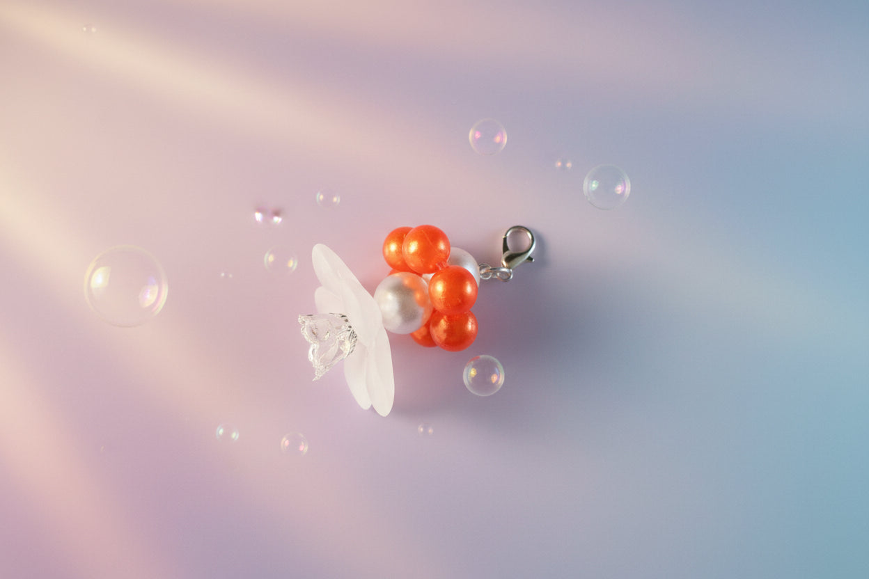 A stunning white flower bead takes centre stage, encircled by shimmering orange pearlescent beads that create a mesmerising spinning effect. The soothing tactile motion helps with focus and stress relief while looking absolutely magical.