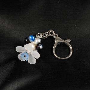 A stunning white flower bead takes center stage, encircled by shimmering dark blue pearlescent beads that create a mesmerizing spinning effect. The soothing tactile motion helps with focus and stress relief while looking absolutely magical.