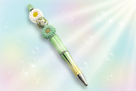 A graduated green to gold metallic pen with a green and a white daisy shaped beads and a round bead with a daisy pattern.