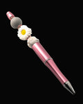 A pink metallic pen with a white daisy shaped bead, a plain grey bead, a pink an grey floral bead with pink rondelles