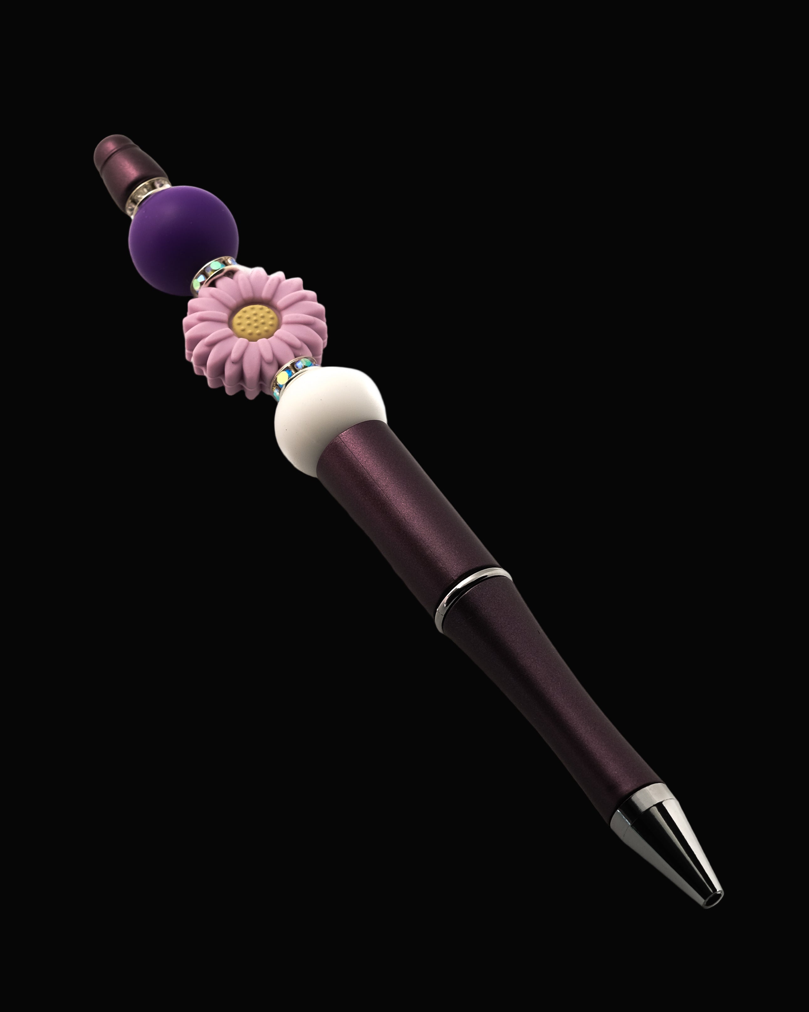 A purple metallic pen with a purple daisy shaped bead, a purple round bead, a white bead and sparkly Rondelle.