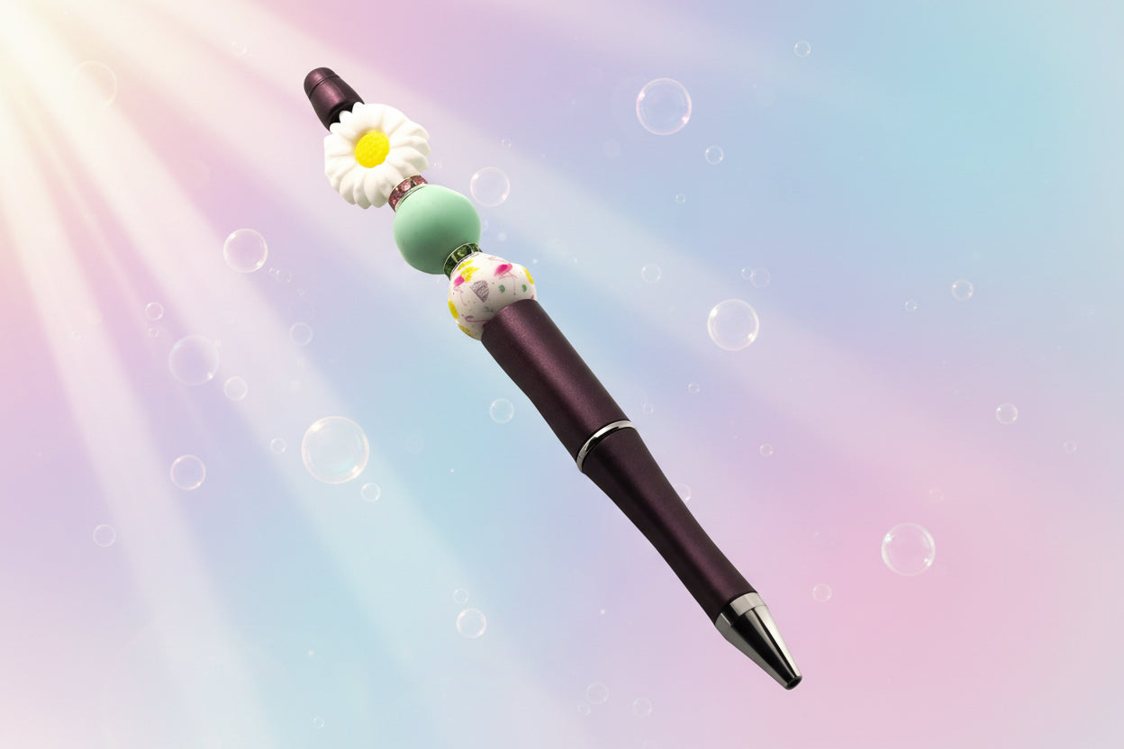 A purple metallic pen with a white daisy shaped bead, a green round bead, a white bead with a floral design and a pink and a green Rondelle.
