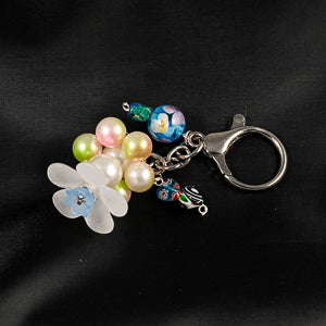 Pink and green pearlescent beads form a circlet beneath a large white flower bead creating a spinner fidget that has a chain with beads and lobster claw that can be clipped to your keychain.