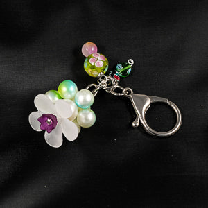  A stunning white flower bead takes center stage, encircled by shimmering green pearlescent beads that create a mesmerizing spinning effect. 