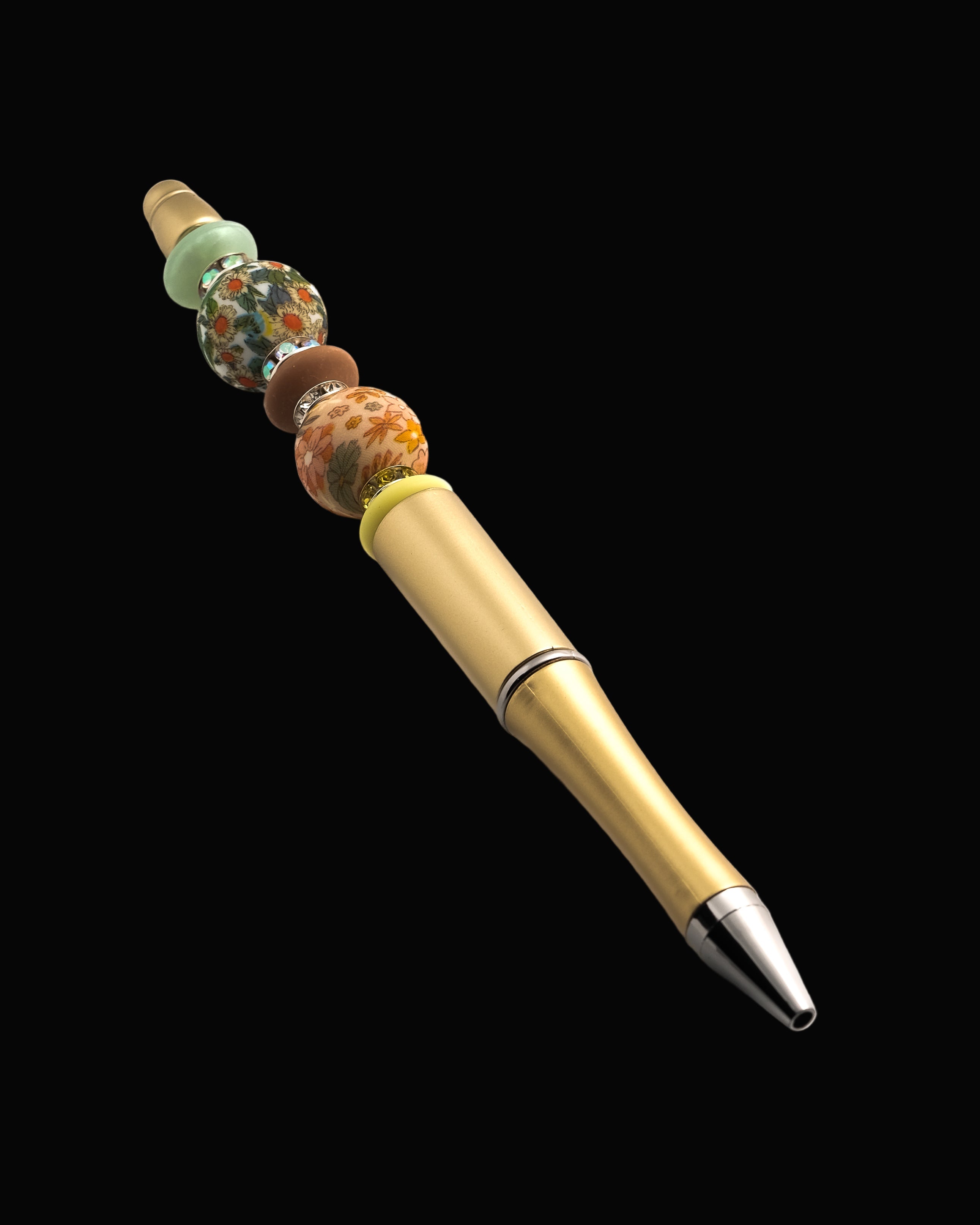 A gold metallic pen with floral beads, a yellow oval bead, a green oval bead, a fawn oval bead and sparkly Rondelles.