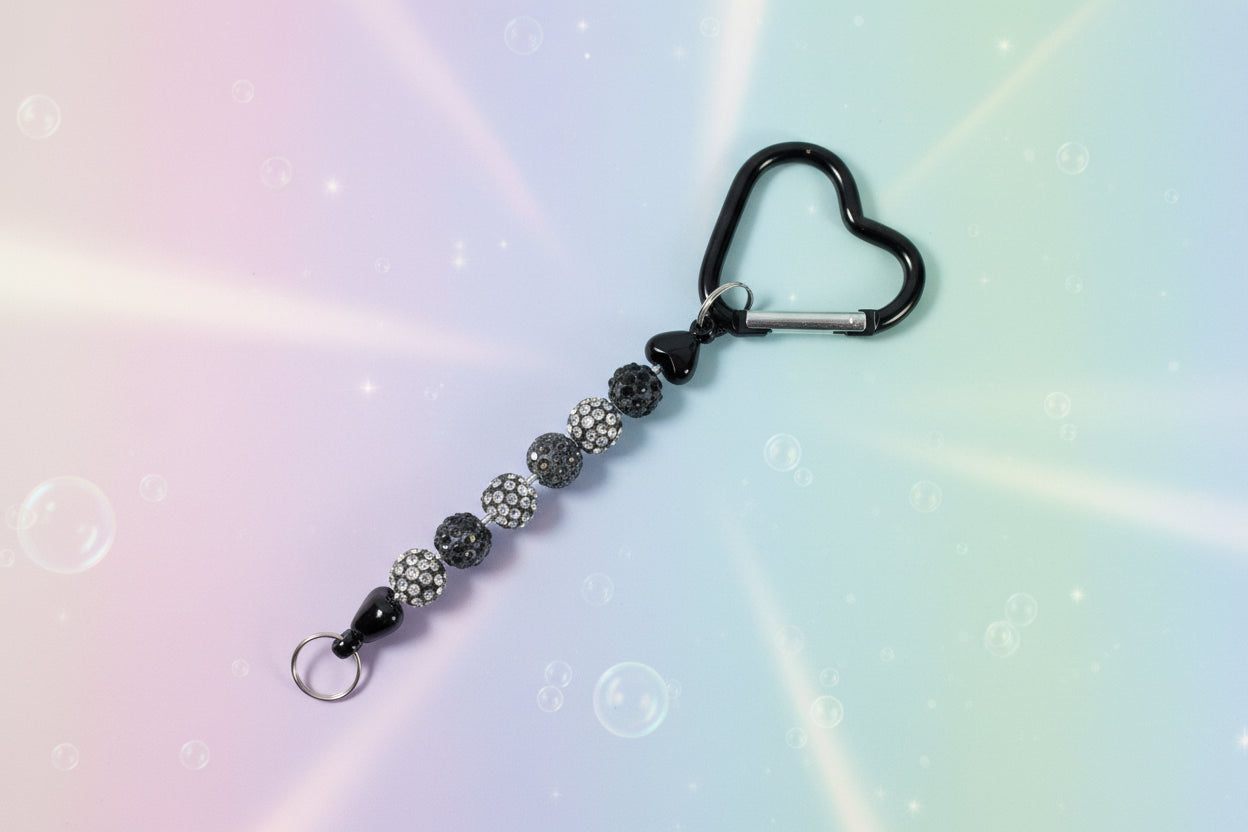 Add a touch of sparkle and love to your everyday essentials with this charming black heart keychain. Adorned with shimmering beads, this delightful accessory brings personality and joy to your keys, bag, or backpack.